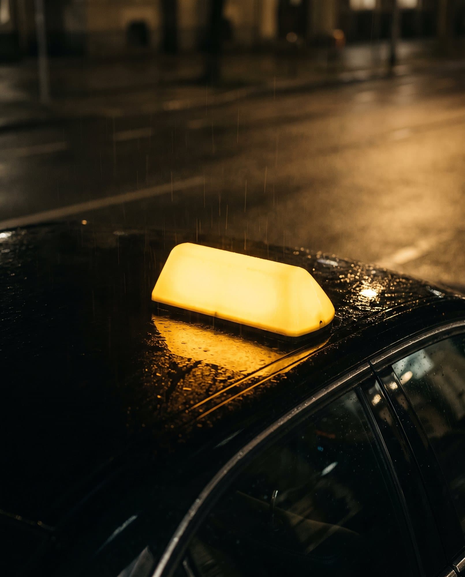Beleuchtetes gelbes Taxi-Dachschild auf einem regennassen schwarzen Wagendach bei Nacht